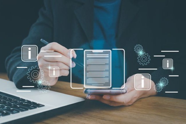 Eine Person sitzt an einem Schreibtisch und gibt Daten in ein Smartphone ein. Das Bild steht für die gemeinsame Arbeit an der digitalen Baugenehmigung.